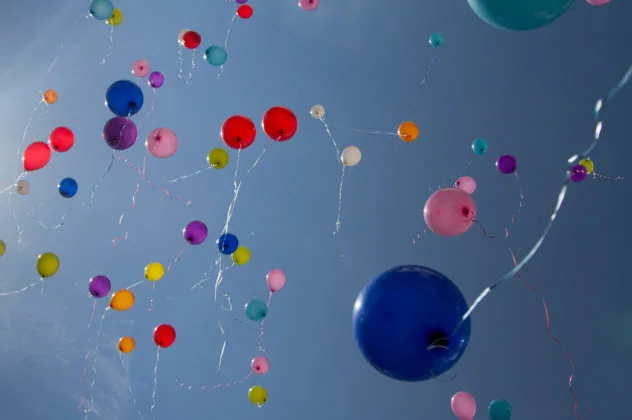 Colorful balloons floating into a blue sky, symbolizing a memorial during lockdown