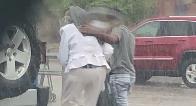 Teenager shielding elderly woman from rain