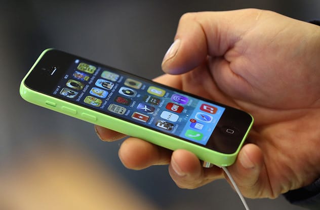 A hand holding a smartphone displaying various app icons on its screen