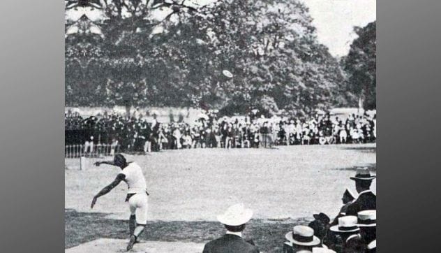 Rudolf Bauer competing in discus at the 1900 Paris Olympics in a grassy, tree-lined area