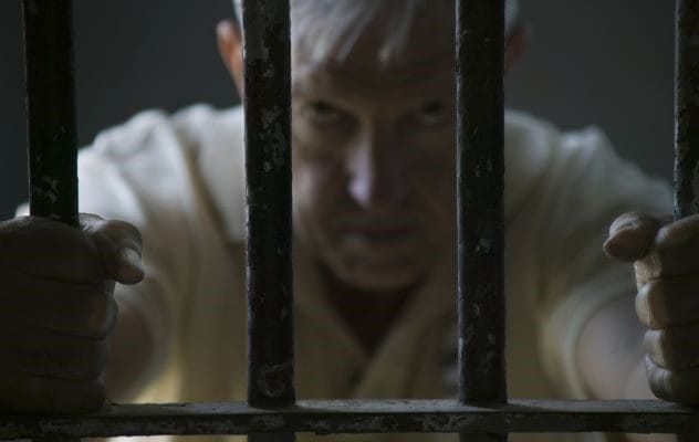 A lone figure walking down a long, empty prison hallway.