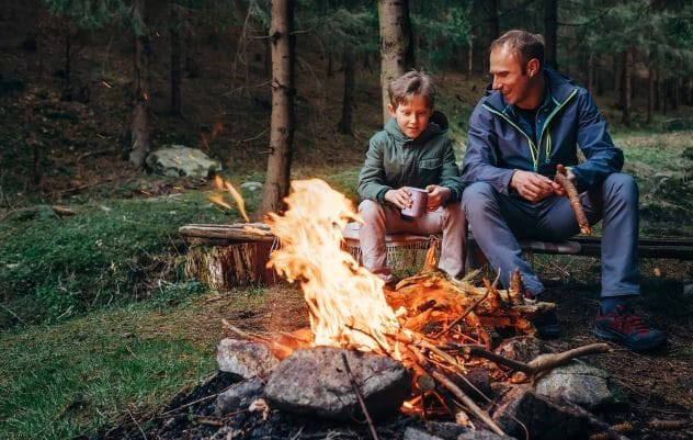 A silhouette of a father and two children hiking in a mountainous area at sunset.