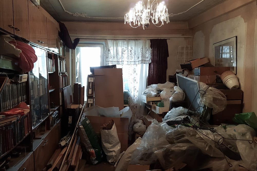 A hoarded room with old food containers and scattered papers