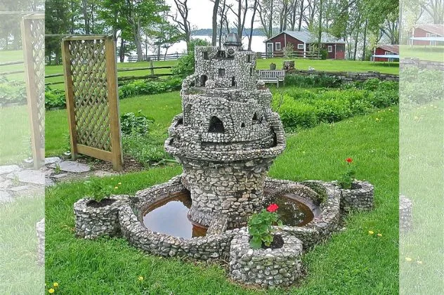 A miniature stone castle with turrets and small windows, nestled in a grassy area with trees in the background.