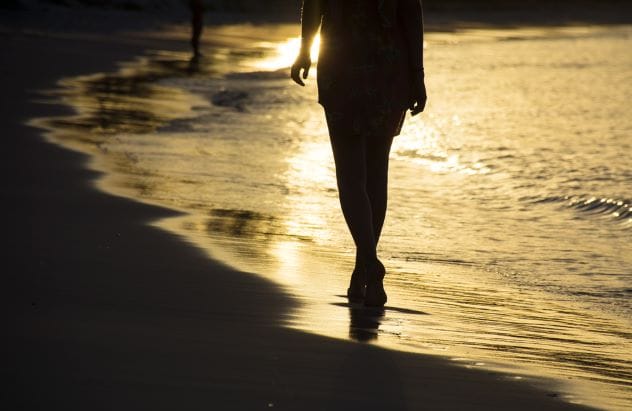 A solitary figure walking on a beach at dusk